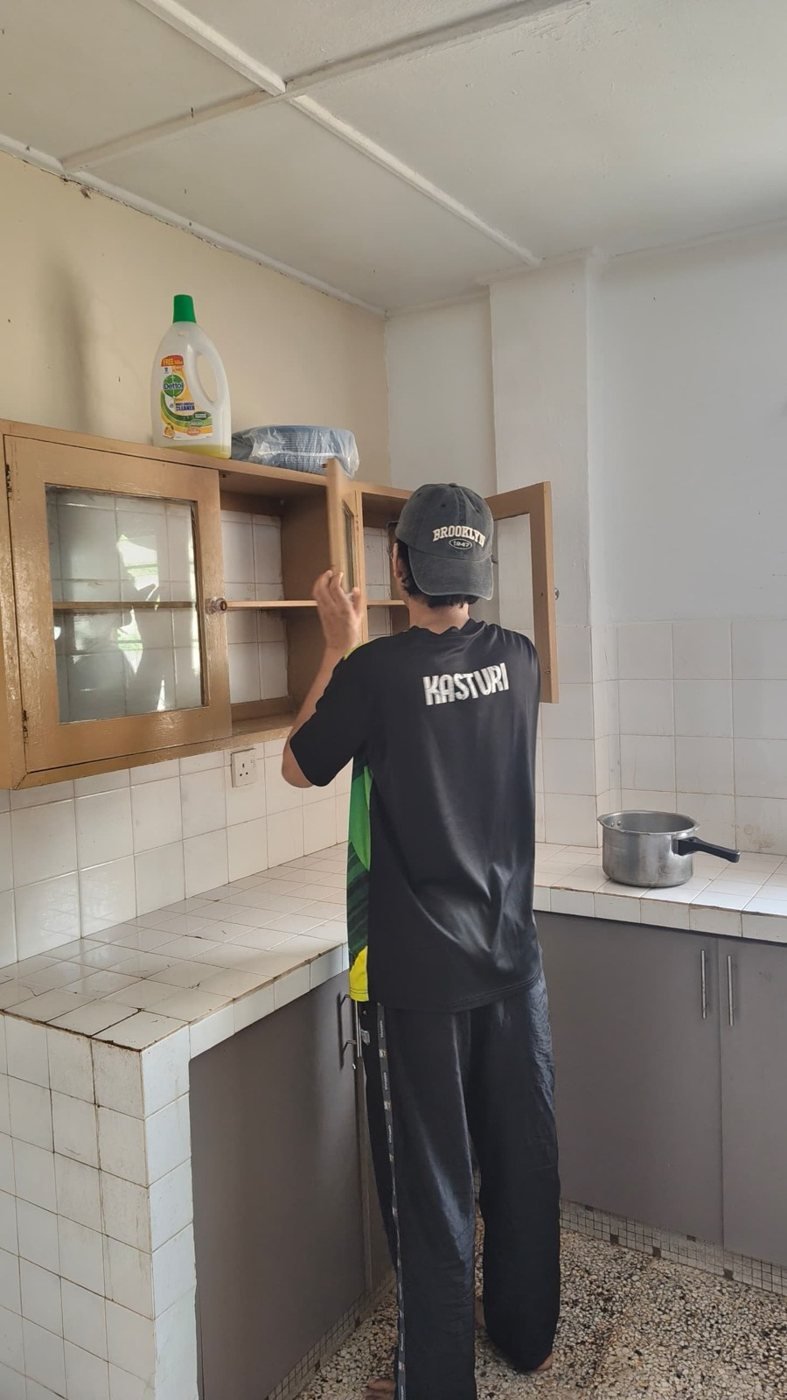A resident cleaning kitchen cabinets, seen from behind
